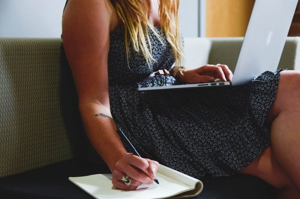 person sitting on a couch and making notes while watching a webinar on business 